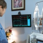 Profissional de saúde observa um monitor com sinais vitais em ambiente hospitalar.