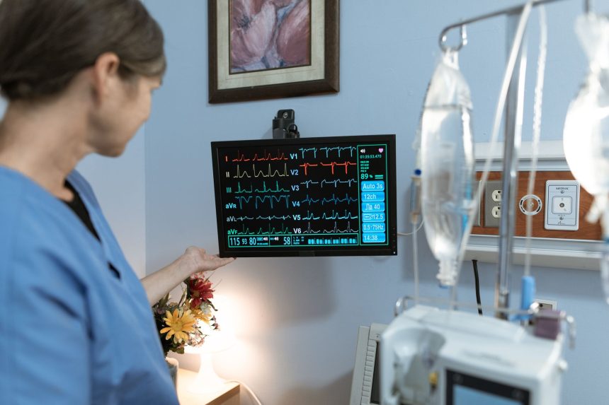 Profissional de saúde observa um monitor com sinais vitais em ambiente hospitalar.