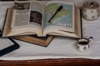 Atlas antigo aberto em um mapa da América do Sul, acompanhado de uma caneta e uma xícara de café.