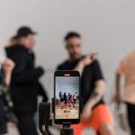 Grupo de dançarinos grava uma apresentação com um smartphone apoiado em um tripé.